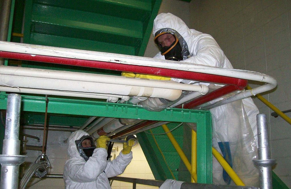 Workers in protective equipment removing asbestos from a federal facility before demolition.